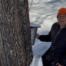 Marilyn beside a maple tree with her hand on a maply syrup bucket